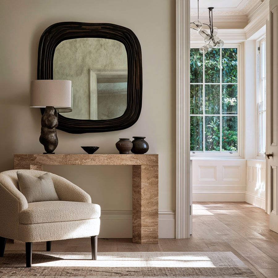 Travertine console with a sculptural lamp and organic dark wood mirror beside a boucle chair