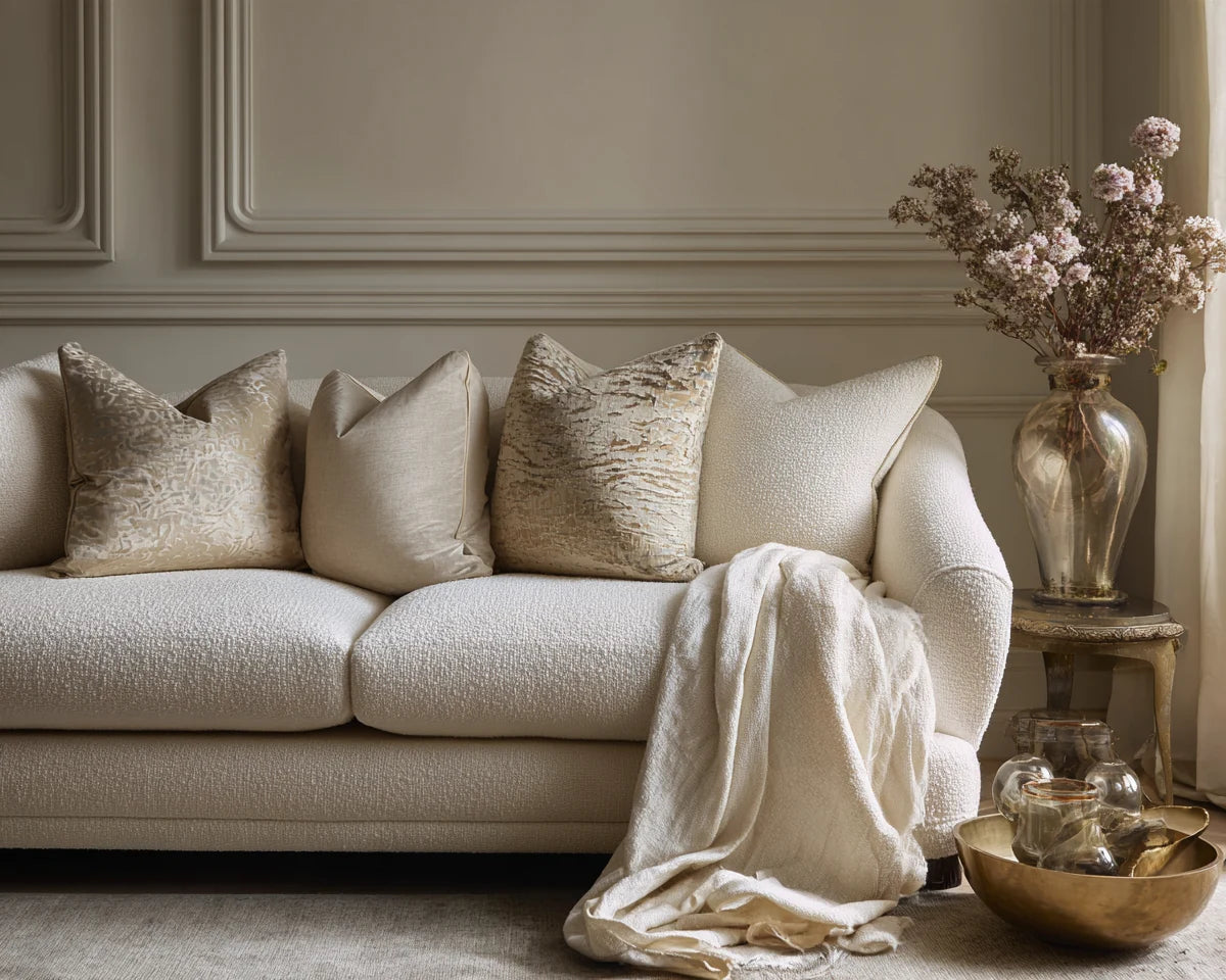 Close-up of luxury cream textured sofa upholstery with layered linen cushions and a soft throw