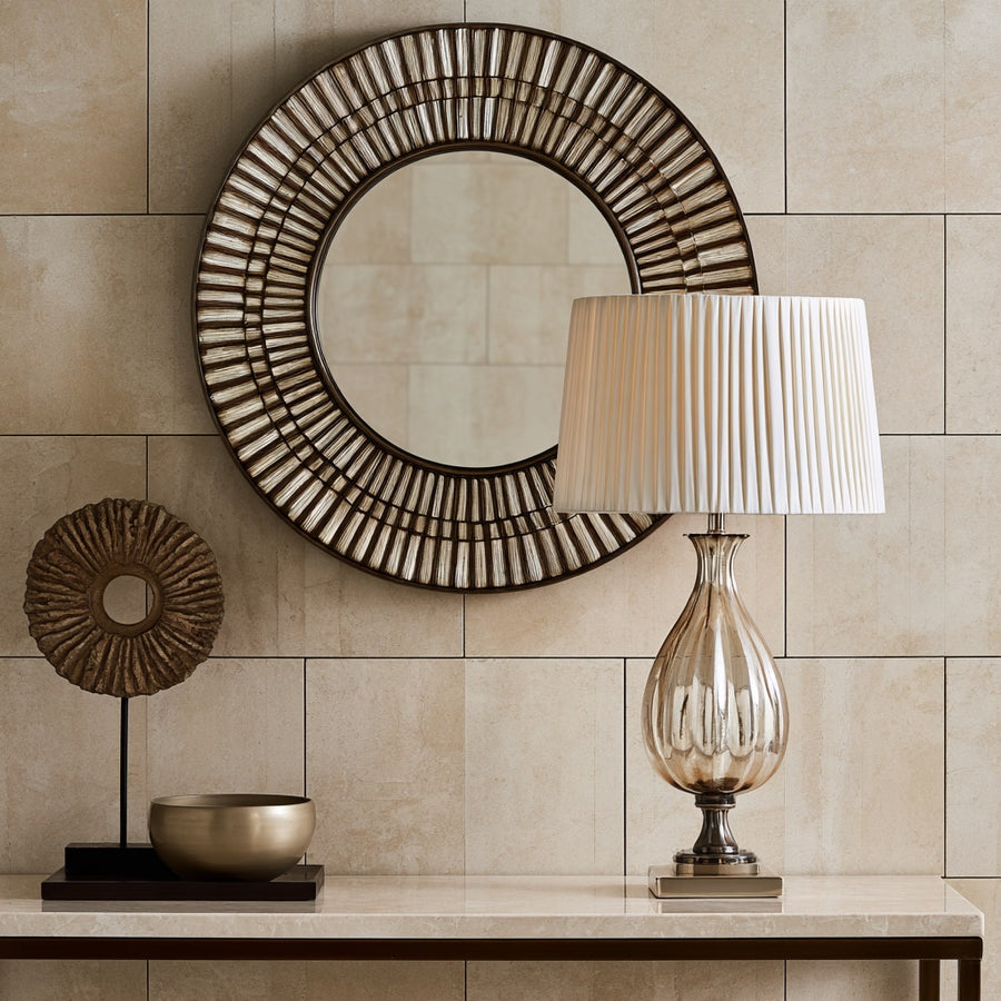 Round ribbed mirror above a console with a glass table lamp and brass bowl