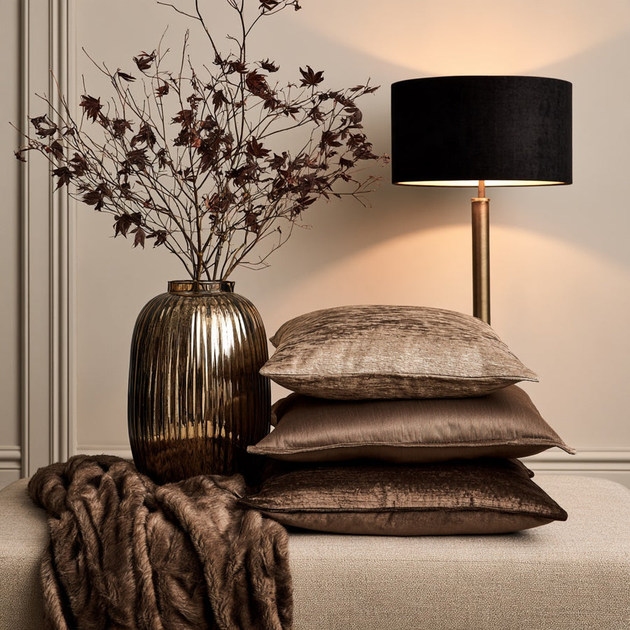 Stacked velvet cushions, faux fur throw and a bronze ribbed vase with a black-shaded lamp